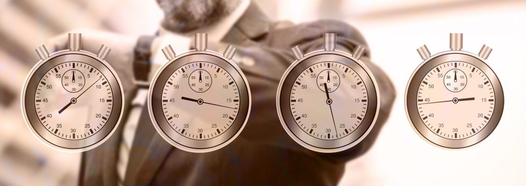 Mężczyzna patrzący na zegarek i cztery zegary wskazujące różne godziny