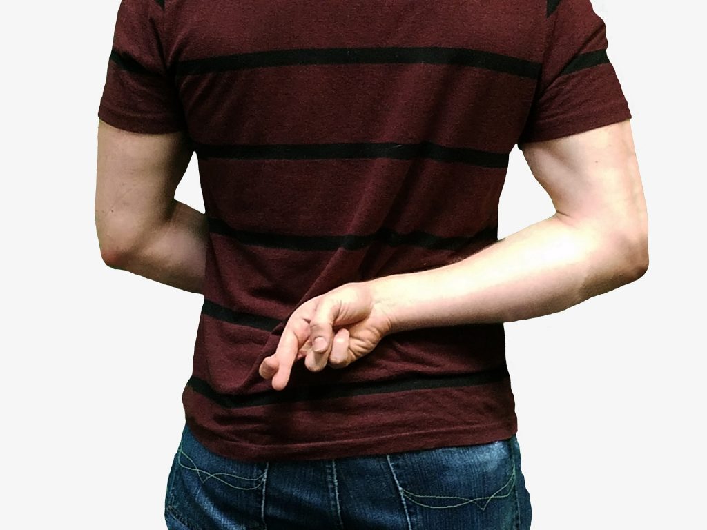 Mężczyzna trzymający za plecami skrzyżowane palce na znak , że okłamuje drugą osobę
